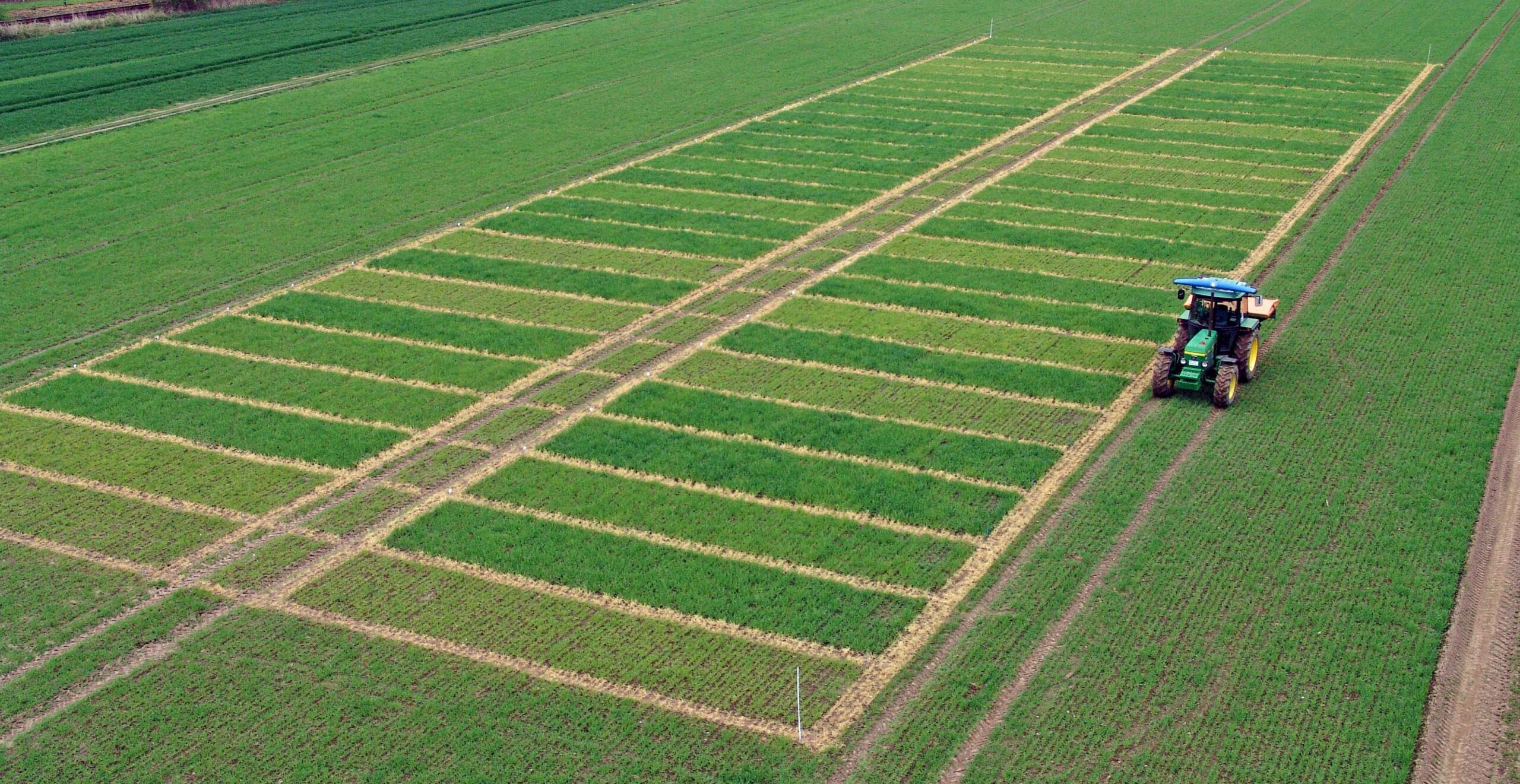 Luftfoto av grønne forsøksruter på et jorde med en traktor som kjører langs feltet til høyre.